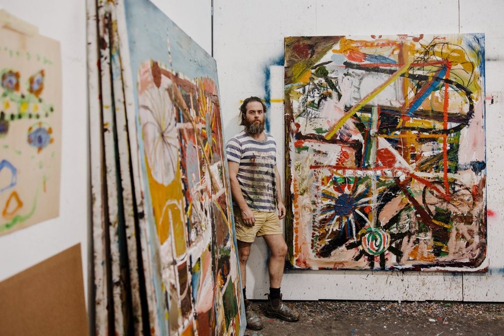 Artist James Drinkwater standing between art work pieces