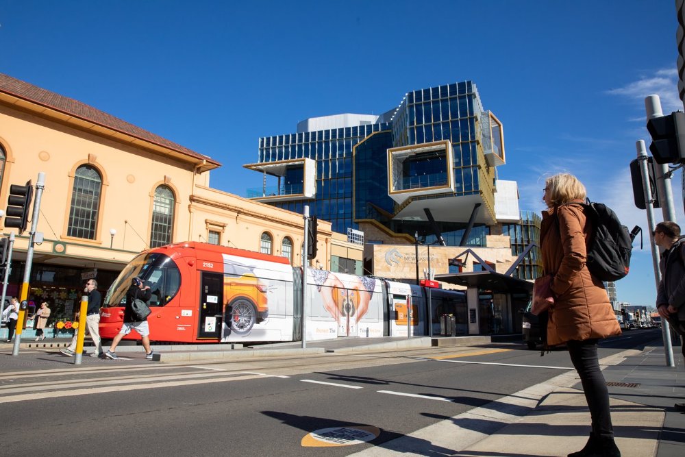 A woman waiting to cross the road as the light rail tram passes by