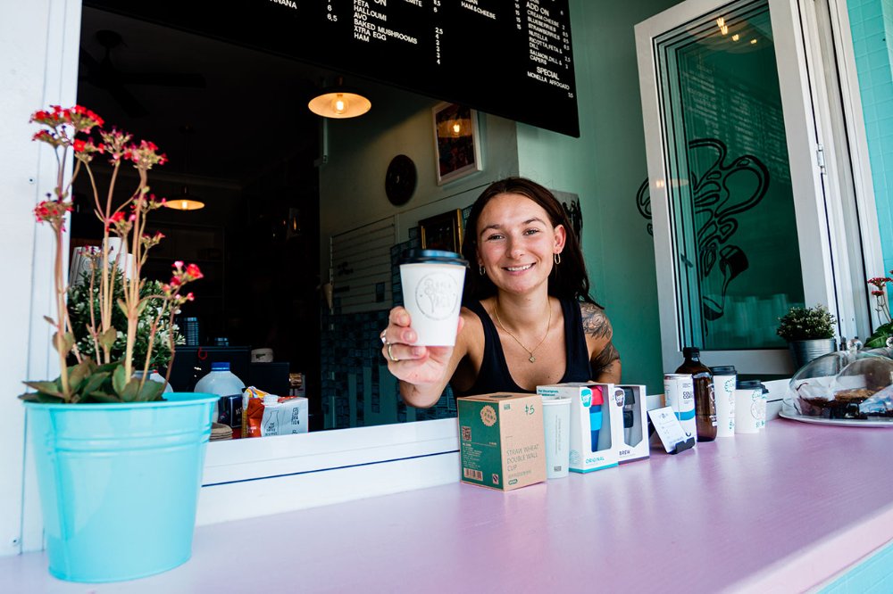 A woman hands coffee out a cafe window