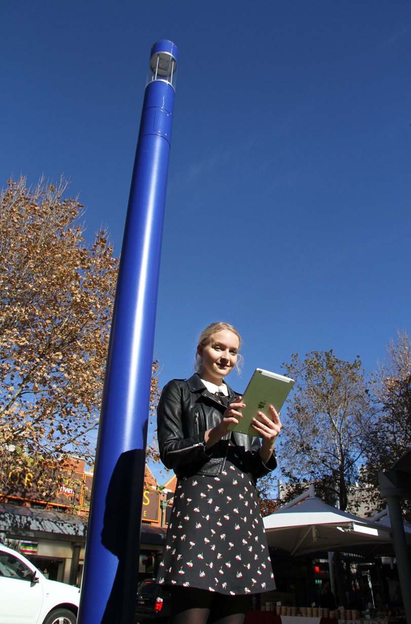 A lady using an ipad in front of a smart pole in Newcastle city
