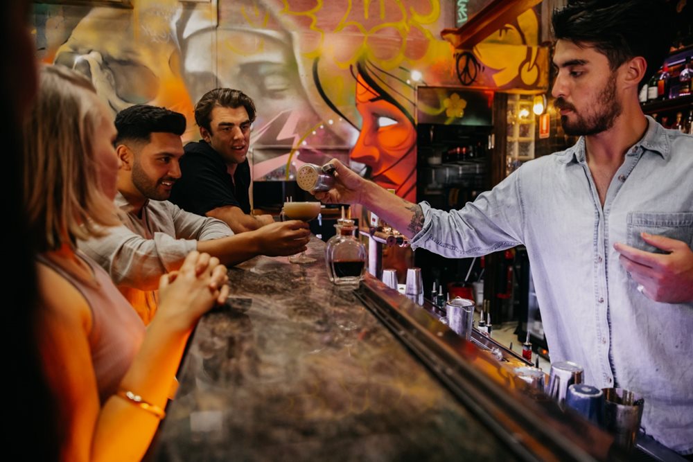 a barman serving guests drinks at a cocktail bar