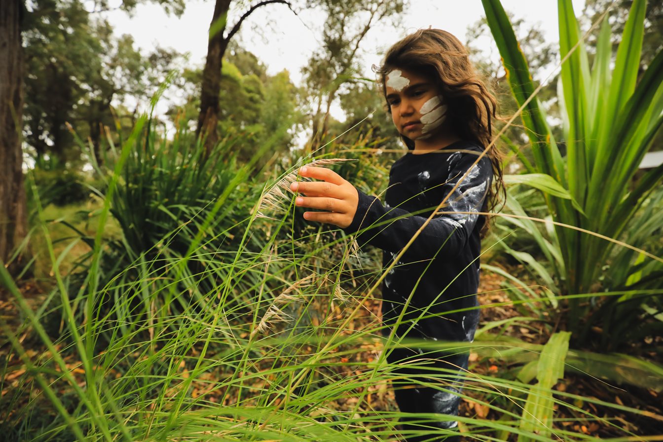 A young girl with face paint touching a plant stem